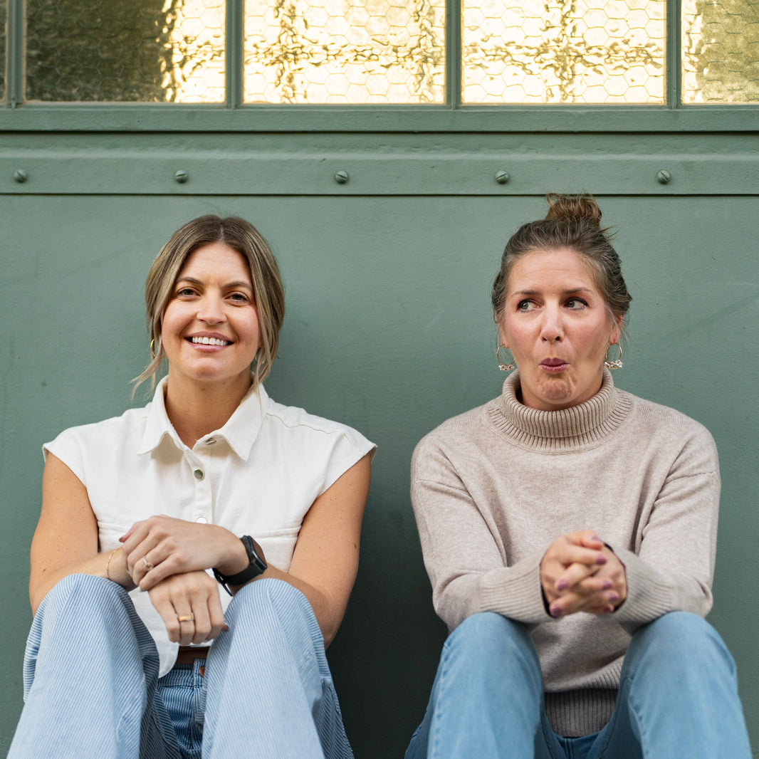 Traci Gorman and Alicia Retzlaff sitting next to eachother in front on a green wall